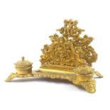 A Victorian rococo style brass desk stand, cast with cherubs, winged beasts and vase of flowers, hav