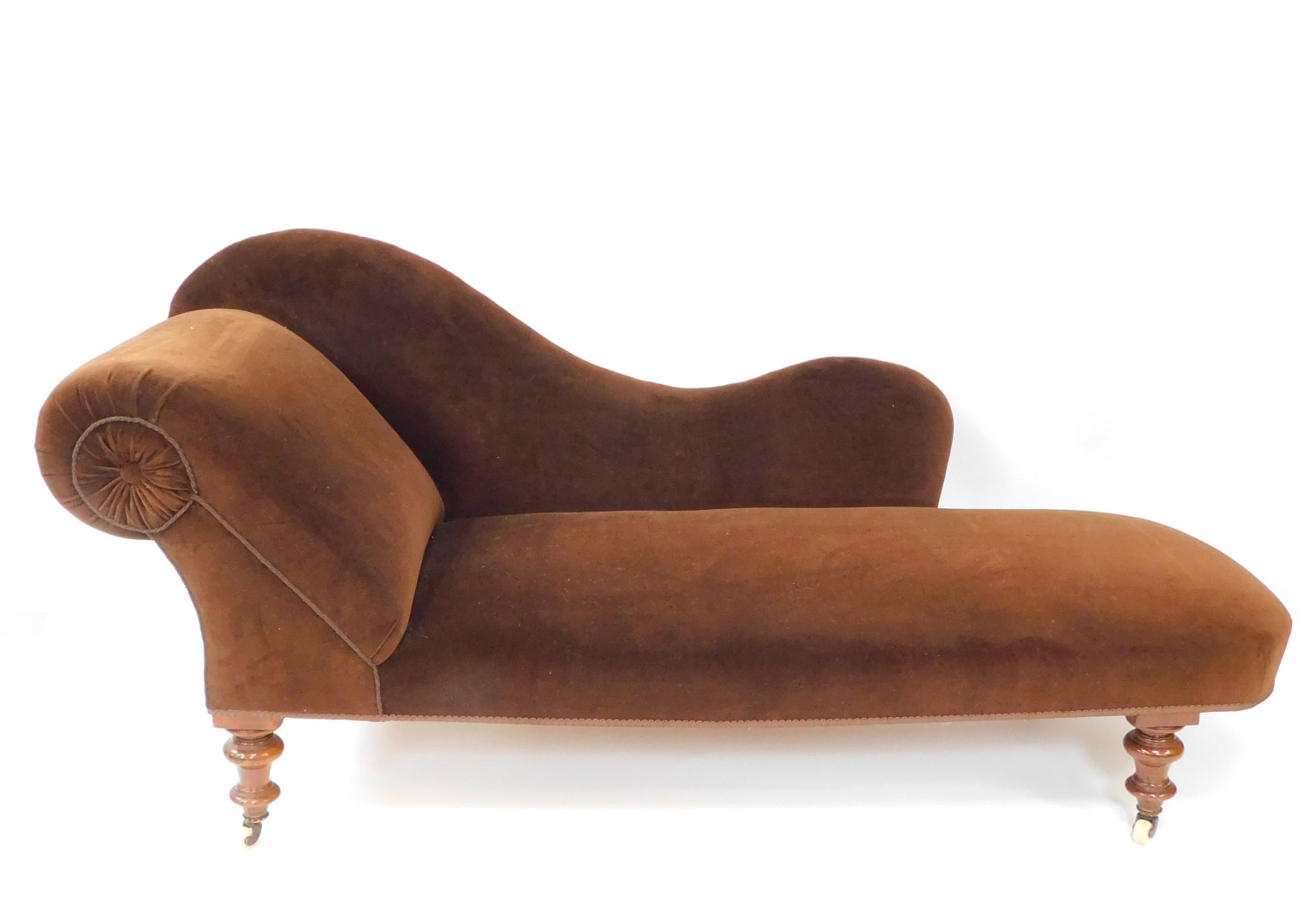 A Victorian mahogany chaise longue, upholstered in brown velour, raised on turned legs, brass capped