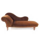 A Victorian mahogany chaise longue, upholstered in brown velour, raised on turned legs, brass capped