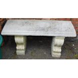 A reconstituted stone garden seat, raised on two scroll supports, 99cm wide.