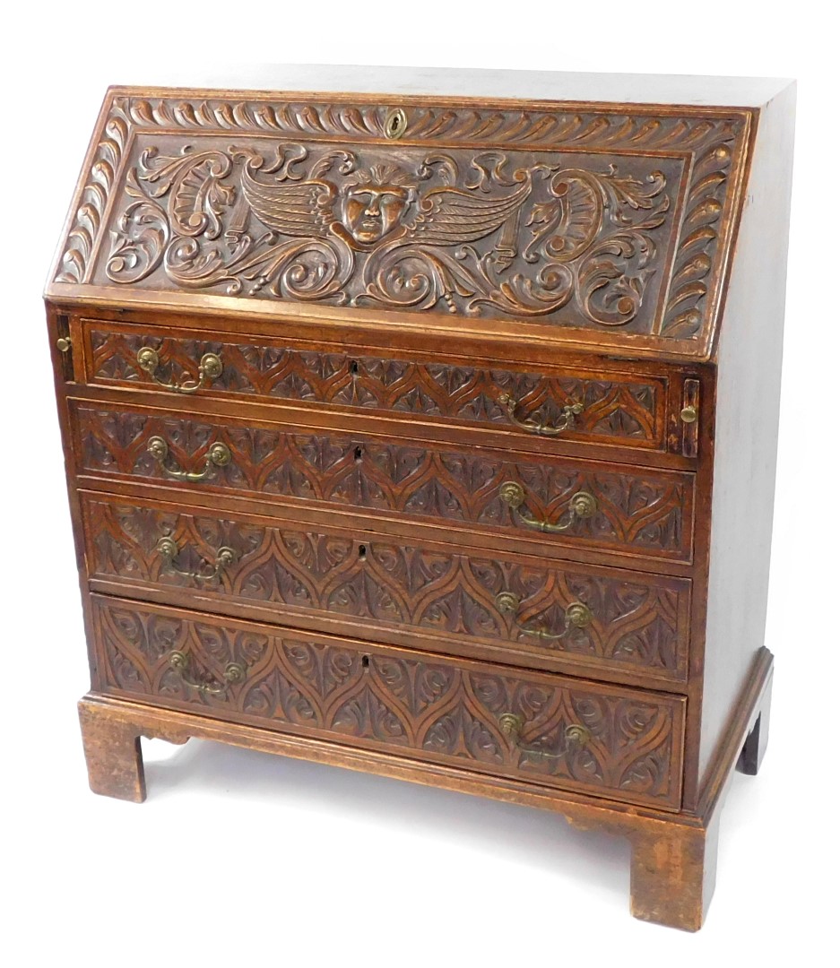 A George III and later carved oak bureau, the fall flap carved with a cherub's head, opening to reve