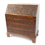 A George III and later carved oak bureau, the fall flap carved with a cherub's head, opening to reve