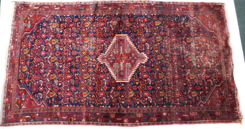 A Persian rug, with a central medallion, surrounded by geometric motifs on a blue ground, 245cm x