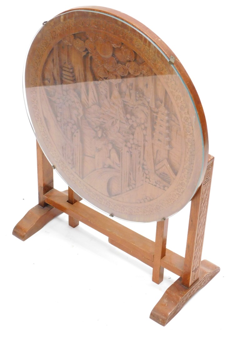 An oriental hardwood occasional table, the circular tilt top carved with figures, buildings,