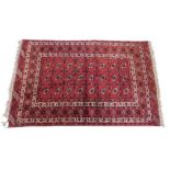 A Bokhara rug, with a typical design of three rows of medallions on a red ground, with multiple