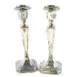 A pair of early 20thC silver candlesticks, with a tapering column and canted square base, loaded,