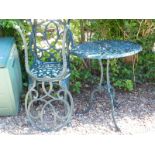 A green metal circular top garden table, and two associated chairs with seat cushions.