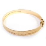 A 9ct gold bangle, with engraved design, of loops and rectangular panels, with safety chain, and sli