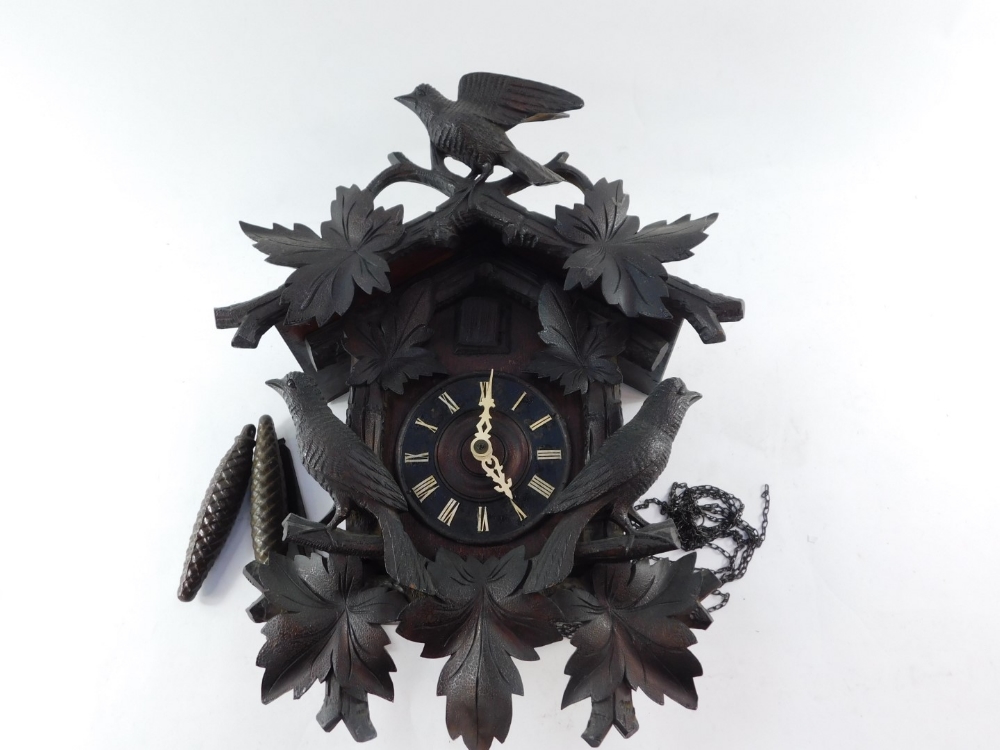 An early 20thC Black Forest cuckoo clock, heavily carved and surmounted by bird and flowers above th