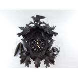 An early 20thC Black Forest cuckoo clock, heavily carved and surmounted by bird and flowers above th