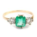 A dress ring, with central rectangular cut emerald in full claw setting, flanked by two round brilli