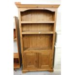 A modern pine bookcase, with cornice top above three shelves and two cupboard doors one lacking