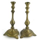 A pair of engraved brass candlesticks, each on a stepped base with tapering feet, 22cm high.
