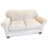 An Edwardian two seater sofa, re-upholstered in floral fabric, on bun feet.