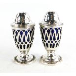 A pair of Victorian pepper pots, each with a pierced body revealing a blue glass liner, on a pedesta