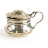 A George VI silver mustard pot, with a bulbous body and hinged lid, revealing a blue glass liner, Bi