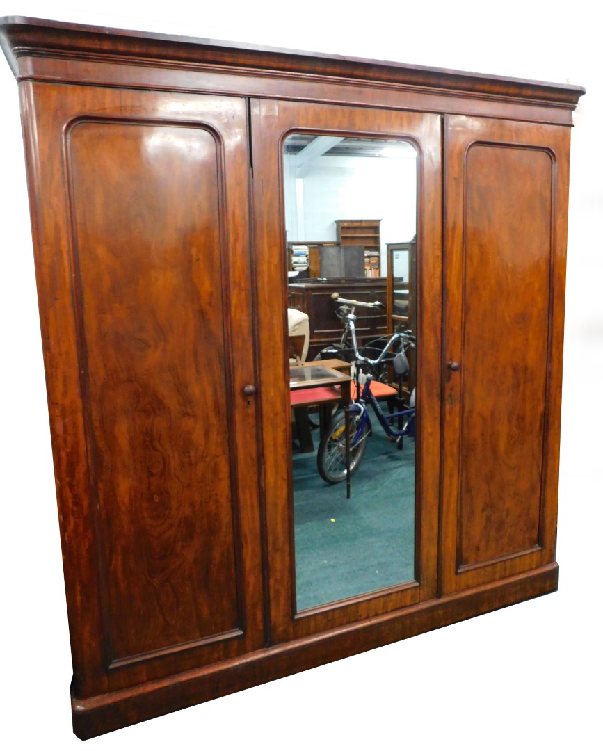 A Victorian figured mahogany triple wardrobe, with a moulded cornice above a central mirror, flanked