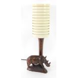 A mid century wooden table lamp carved with a rhinoceros, with a banded cream plastic cylindrical sh