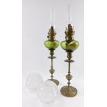 A pair of early 20thC brass oil lamps, with cast candlestick bases, ribbed green glass reservoirs, c