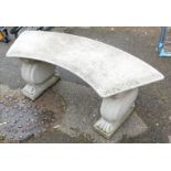 A reconstituted stone curved garden bench, raised on scroll ends supports.