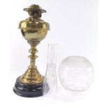 An early 20thC brass oil lamp, raised on a turned black socle, with chimney and etched globular glas