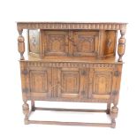 A Jacobean style oak court cupboard, the upper section with double cupboards, beneath a carved canop