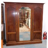 An Edwardian mahogany triple wardrobe, with a mirrored door and panel doors, on a plinth, label to i