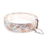 A silver and rose gold plated bangle, engraved and embossed with a bird, butterfly, flowers and leav