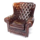 A brown leather wing back Chesterfield armchair, with buttoned decoration and studded borders. The u