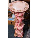 A jardiniere stand, in pink decorated with applied flowers, scrolls etc.