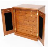 A teak jewellery cabinet, with two single cupboard doors opening to reveal an arrangement of short a