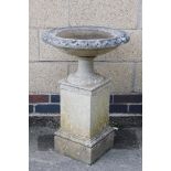 A reconstituted stone bird bath, the circular bird bath top with fluted column supports on a block b