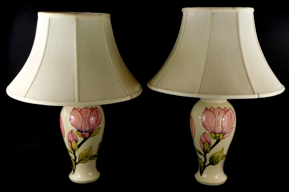A pair of Moorcroft Magnolia pattern lamp bases, each decorated with pink flowers on a cream ground,