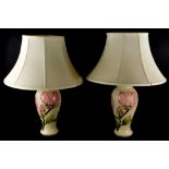 A pair of Moorcroft Magnolia pattern lamp bases, each decorated with pink flowers on a cream ground,