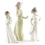 Three Nao porcelain figurines, one holding a pink flower, one a puppy and a girl holding her dress.
