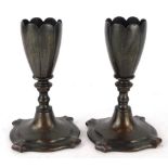 A pair of bronze petalled candle stands, each with a ribbed top on shaped square base 13cm high.