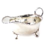 A George V silver sauce boat, with a scroll cast rim, shaped handle, on three supports, Birmingham 1
