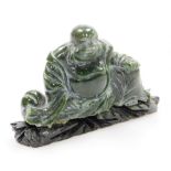 A Chinese carved green hardstone figure of a seated Putai, carved wood stand, 10cm high, 14cm wide.