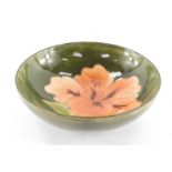 A Moorcroft pottery dish decorated in the Coral Hibiscus pattern, against a green ground, impressed