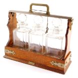 An early 20thC oak and silver plated tantalus, with three square section decanters, each with facete