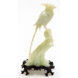 A carved jade sculpture of a long tailed pheasant perched on branch, on carved and lacquered hardwoo