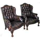 A pair of Chesterfield style wing back armchairs, each upholstered in a brown studded leather, with