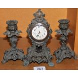 A cast metal mantel clock and two matching candlesticks.