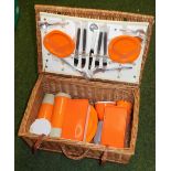 A wicker picnic basket and contents, with orange plastic wares, marked Travel With Safety.