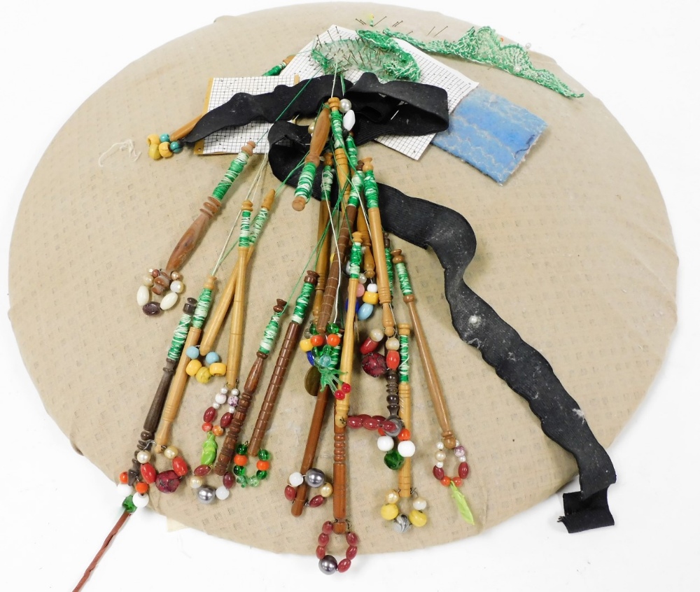 A lace makers pin cushion with various lace bobbins, wooden with beaded ends.