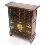 A Chinese hardwood and brass side cabinet, with an arrangement of small drawers and two doors, each