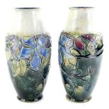 A pair of early 20thC Royal Doulton stoneware vases, tube lined with flowers on a mottled blue groun