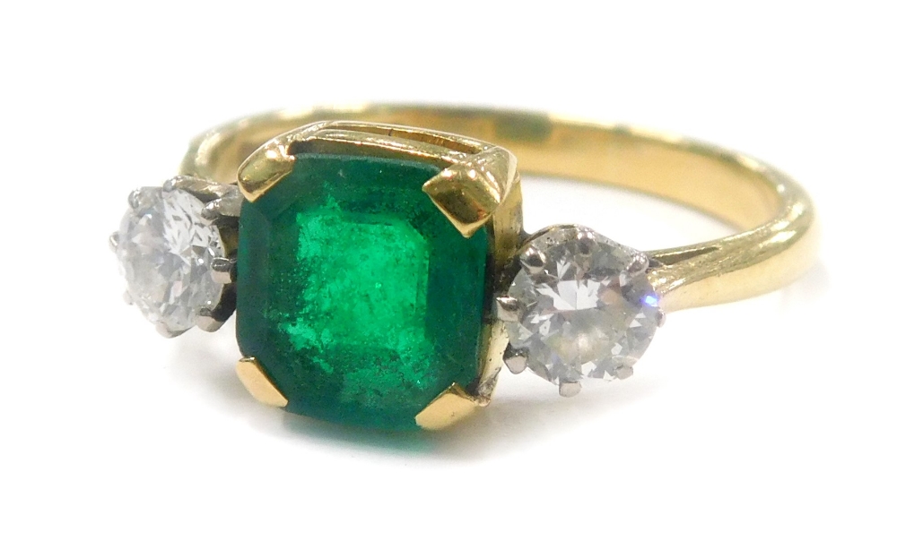 A dress ring, with central square cut green stone, in claw setting, flanked by two round brilliant c