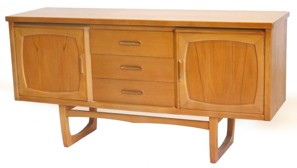 A 1970s teak sideboard, with an arrangement of three drawers, flanked by two panelled doors on shape