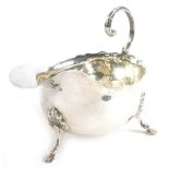 A late Victorian silver sauce boat, with a shaped rim and open scroll handle, raised on three hoof f